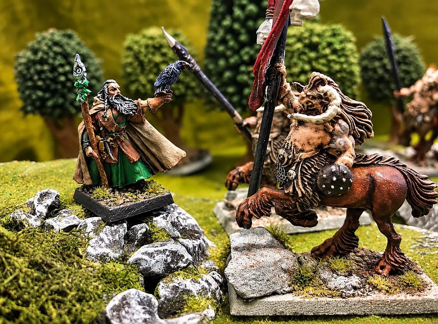 A hand-painted druid with a raven and a centaur miniature on a woodland tabletop battlefield