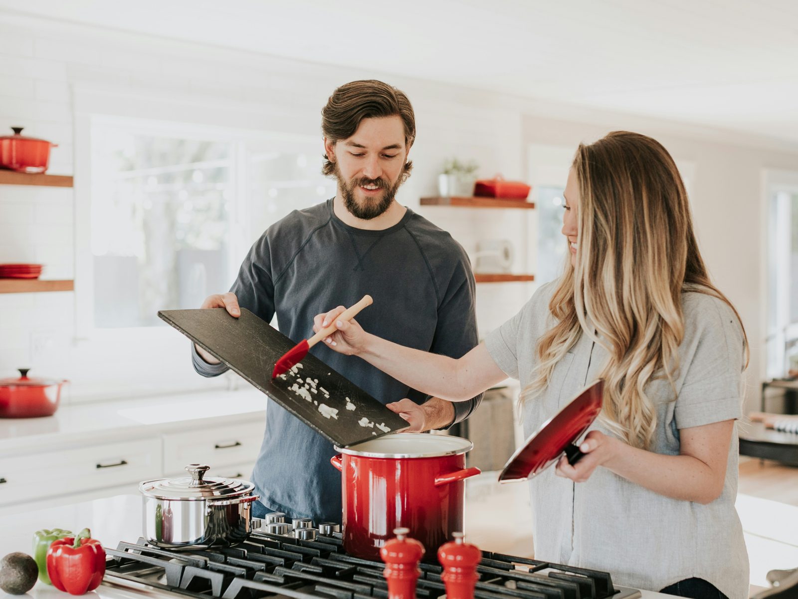 Two people cooking together at a kitchen stove, adding chopped ingredients to a pot